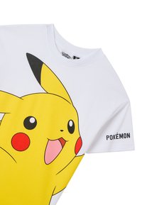 T-shirt bianco in cotone con una grande grafica di Pikachu gialla, guance rosse e testo "POKÉMON" stampato sulla manica. Maniche corte, collo rotondo.