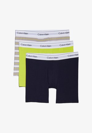 Tres pares de calzoncillos tipo boxer: negros, verde brillante y gris con rayas blancas. Cada uno presenta una pretina blanca con la marca Calvin Klein.