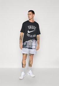 Sort bomulds t-shirt med hvid grafisk tekst, parret med grå mesh shorts med et pixelmønster. Båret med hvide sneakers.
