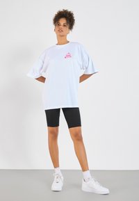 White oversized t-shirt with a pink cupcake graphic on the left chest, paired with black bike shorts and white sneakers.