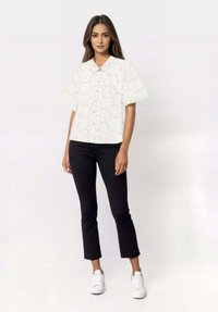 White short-sleeve shirt with a collared neckline featuring embroidered eyelet details, paired with black cropped pants and white sneakers.
