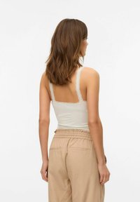 Top bianco senza maniche con spalline in pizzo abbinato a pantaloni beige a vestibilità ampia. La texture liscia e il design aderente aumentano il comfort.