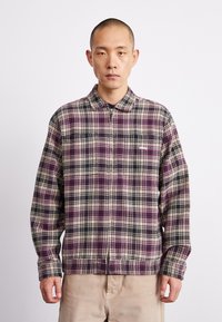 Cămașă în carouri din flanel în nuanțe de violet, negru și bej; mâneci lungi; guler cu butoni; are un fermoar pe față și detalii cu logo.