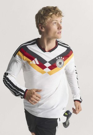 Maillot de football à manches longues blanc avec des rayures noires, des accents diagonaux rouge et jaune, un col en V et un logo sur la poitrine.