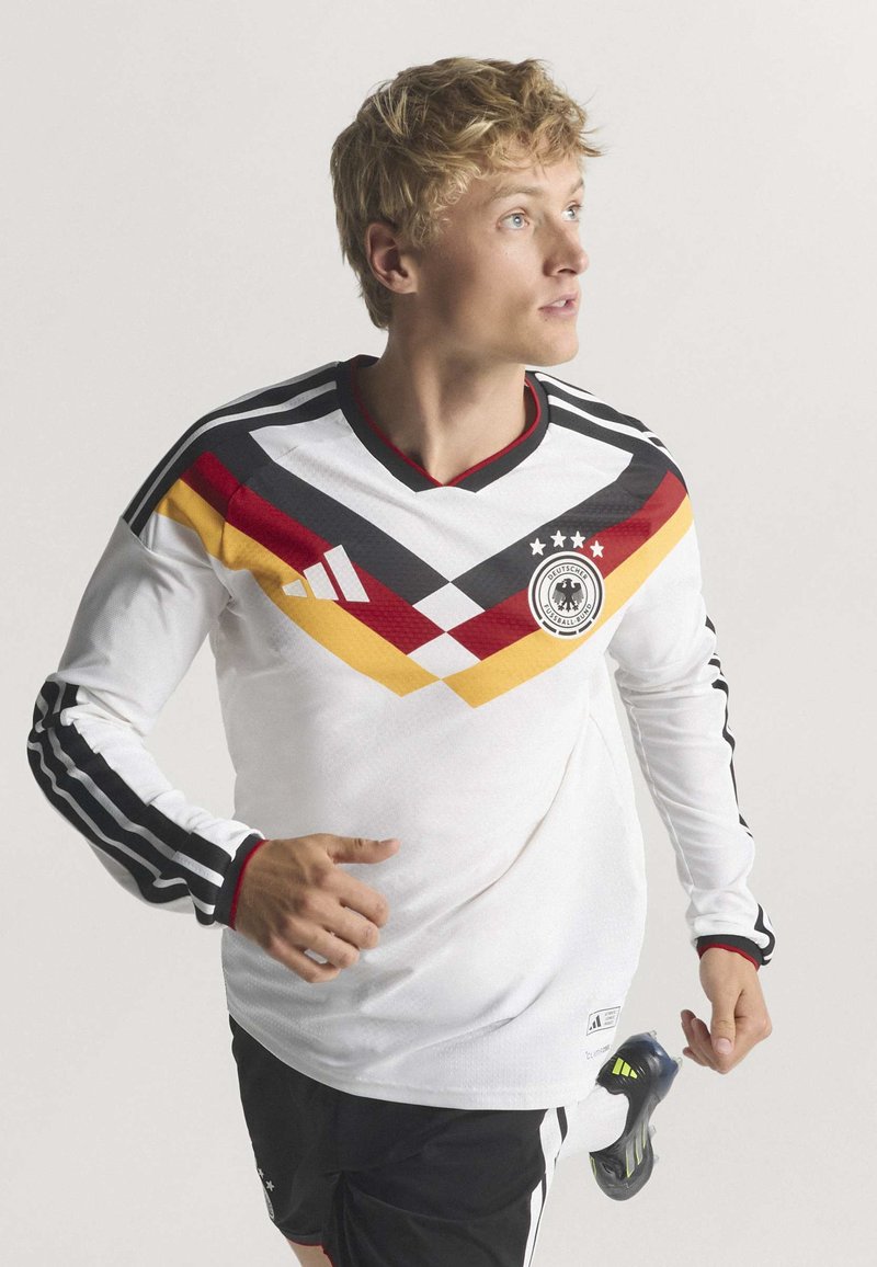 White long-sleeve soccer jersey featuring black stripes, red and yellow diagonal accents, a v-neck design, and a logo on the chest.
