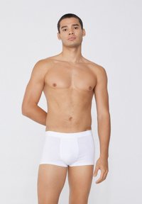 Boxer briefs de algodón blanco con una cinturilla suave y bolsa frontal, exhibidos en un modelo masculino sobre un fondo neutral.