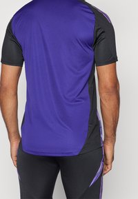 Lila träningsskjorta med svarta sidor, korta ärmar och lila randiga detaljer. Tillverkad av ett smidigt, lätt tyg.