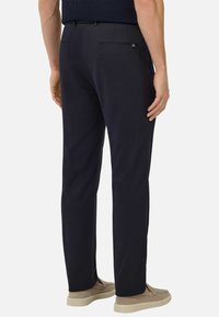 Navy trousers made of cotton blend, featuring a straight cut, back pockets with zippers, and a smooth texture, paired with beige shoes.