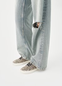 Snake-print sneakers with black laces and a white sole, paired with light blue wide-leg ripped jeans. Texture appears smooth with frayed edges.