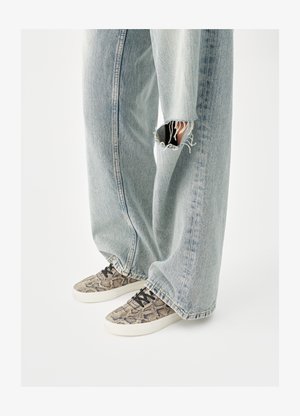 Tenisice s uzorkom zmijske kože, crnim vezicama i bijelim potplatom, uparene s širokim trapericama svijetloplave boje s poderotinama. Tekstura izgleda glatko s izraženim rubovima.