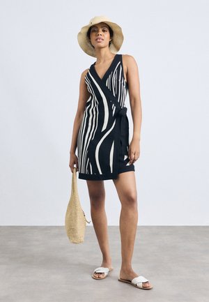 Fekete-fehér csíkos melltartós ruha V-nyakkivágással, megkötős derékkal és térd alá érő hosszúsággal. Woven táskával és fehér szandálokkal párosítva.