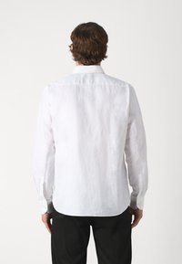 Camicia bianca in lino con maniche lunghe, polsini abbottonati e colletto classico. La vista posteriore mostra un orlo leggermente curvato e nessun motivo visibile.