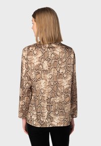 Blusa a maniche lunghe con stampa a serpente, caratterizzata da tonalità di marrone e beige, texture liscia e una vestibilità rilassata con orlo arrotondato.