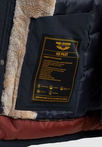 Veste d'hiver bleu marine à l'intérieur en fausse fourrure, étiquette d'entretien bien visible en jaune et noir, avec poches zippées et poches à la main.