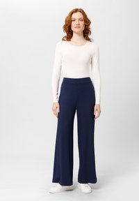 Bodysuit ligero de manga larga en color crema y pantalones de pierna ancha de rayas en color marino con una cintura alta. El modelo lleva zapatillas deportivas blancas.