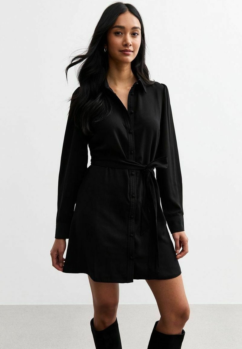 Vestito camicia nero con maniche lunghe, chiusura a bottoni davanti e una cintura in vita. Realizzato in tessuto morbido, presenta un colletto e tasche laterali.