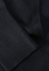 Tissu tricoté noir avec une texture lisse, présentant des coutures et des plis qui affichent un tombé souple. Le matériau est léger et flexible.