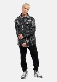 Sort mønstret skjorte med to brystlommer, der har abstrakte design i grå nuancer. Kombineret med sorte bukser og mønstret høj-top sneakers.
