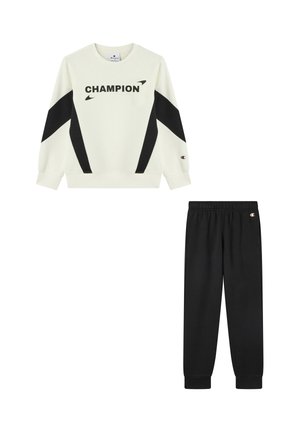 Felpa a maniche lunghe bianca e nera con la scritta "CHAMPION" abbinata a pantaloni jogger neri con vita elastica, entrambi con toppe del logo Champion.