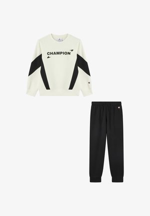 Biała i czarna bluza z długim rękawem z napisem "CHAMPION" w połączeniu z czarnymi dresowymi spodniami z elastycznym pasem, obie części z naszywkami z logo Champion.