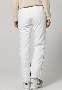 Witte skibroek met een aansluitend ontwerp, zwarte strepen aan de zijkant, een gladde textuur en sneeuwlaarzen met zichtbare merkdetails.