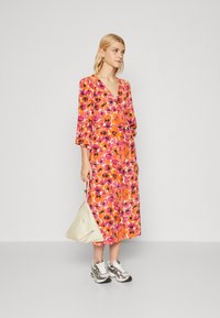 Blommönstrad klänning i rosa och orange nyanser, med v-ringning, trekvartslånga ärmar och en lös passform. Matchad med silversneakers och en beige väska.