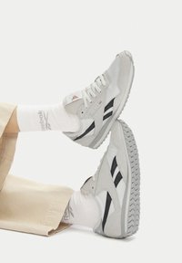 Jasnoszare sneakersy wykonane z połączenia gładkiego i zamszowego materiału, z czarnymi paskami i teksturowanymi kauczukowymi podeszwami. W komplecie z białymi skarpetkami.