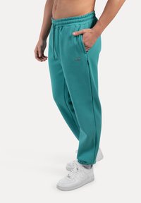 Turquoise sweatpants met een elastische tailleband, zijzakken en contrasterende hardwareaccenten, gecombineerd met witte sneakers.