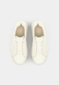 White leather sneakers with a smooth texture, round toe, lace-up closure, and minimalistic design. Branding on the tongue visible.