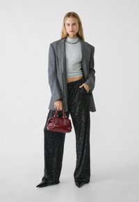 Grå oversized blazer, ribbet lysegrå crop top, sorte glitrende vide bukser og en lille burgunder håndtaske med to håndtag. Sorte spidse sko.