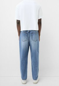 Jeans de mezclilla azul con un corte relajado, que presentan dos bolsillos traseros, un leve desgaste y se combinan con una camiseta blanca corta sencilla.