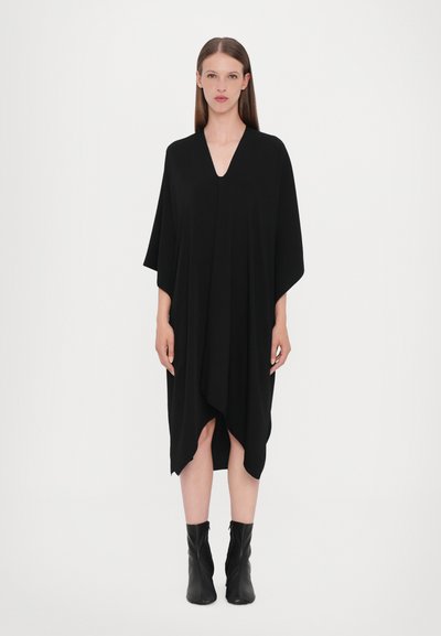 Abito nero fino al ginocchio con scollatura a V e maniche ampie, caratterizzato da un design drappeggiato e un orlo asimmetrico. Texture liscia e stile minimalista.