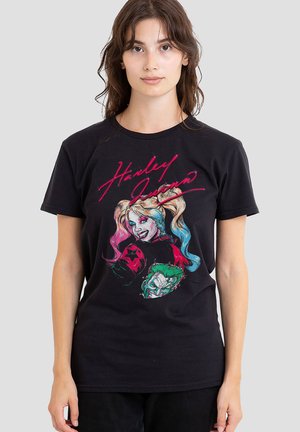 Woman wearing a black t-shirt with colorful Harley Quinn and Joker illustrations and "Harley Quinn" text in pink script.