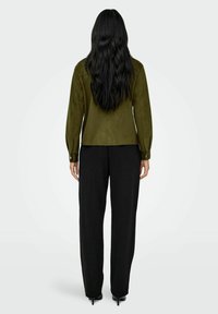 Green suede jacket with a tailored fit, long sleeves, and buttoned cuffs, paired with black wide-leg trousers. Smooth texture.