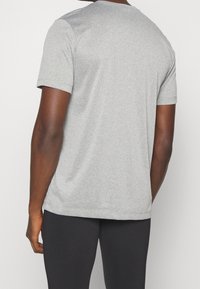 Grå kortärmad sporttröja med rund halsringning, tillverkad av ett mjukt och lätt tyg, visad på en person som bär svarta leggings.