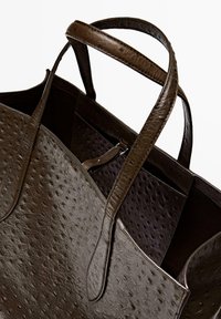 Brown leather tote bag featuring a textured surface, dual sturdy handles, and an open top design. Interior has a pocket for organization.