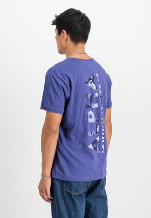 Lila Baumwoll-T-Shirt mit einem großen, vertikal ausgerichteten Alpha-Graphic im Camouflage-Print. Kurze Ärmel und Rundhalsausschnitt.