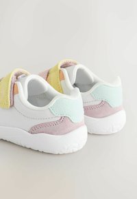 White sneakers with pastel accents in yellow, pink, and blue suede. Velcro strap, rounded shape, textured soles.