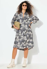Grå blomster skjortekjole med lange ærmer, knaplukning foran og asymmetrisk kant. Parret med cremede snørebåndsstøvler og en lysebrun clutch.