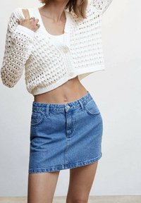 Witte gebreide cropped cardigan met knopen, gecombineerd met een lichtblauwe denim mini-jurk met voorzakken en een rafelige zoom.