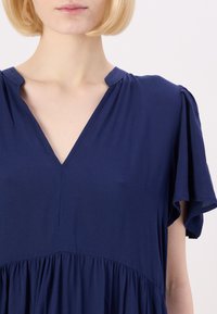 Abito blu navy con scollo a V, maniche a sbuffo corte e gonna arricciata. Realizzato in un tessuto morbido e liscio. Design minimalista senza motivi.
