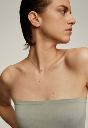 Collarín de plata con un pequeño colgante, llevado sobre hombros desnudos, contrastando con una blusa strapless gris claro y una textura de piel suave.