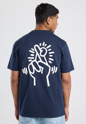 Camiseta de algodón azul marino con un gráfico blanco de una mano con los dedos cruzados y líneas radiales en la parte posterior. Manga corta, corte relajado.