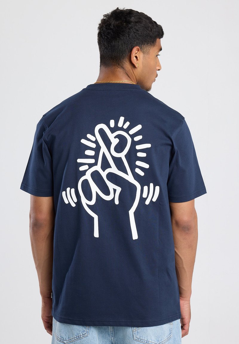 Camiseta de algodón azul marino con un gráfico blanco de una mano con los dedos cruzados y líneas radiales en la parte posterior. Manga corta, corte relajado.