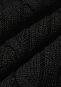 Czarna dzianina o fakturowanym wzorze, z widocznymi skręconymi włóknami i prążkowanymi fragmentami, ukazująca szczegóły nachodzących na siebie warstw.