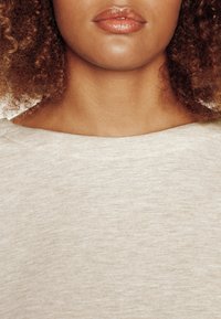 Haut beige clair avec un large décolleté dégagé, fabriqué à partir d'un tissu doux et texturé. Présente une finition lisse et des détails de couture minimaux.