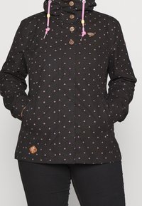 Czarna kurtka w kwiatowy wzór w różowym kolorze, z zamknięciami na guziki, regulowanym kapturem z różowymi sznurkami oraz brązową naszywką.