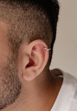 Silberner Creolenohrring, der am Lobe eines kurzgeschnittenen männlichen Ohres mit kurzem Haar befestigt ist und eine glatte, polierte Oberfläche aufweist.