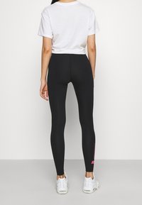 Svarta leggings med hög midja, tillverkade av elastiskt material, tillsammans med en vit t-shirt med kort ärm och vita sneakers.