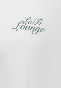 Text "Lo Fi Lounge" in dunkelgrüner Schreibschrift auf weißem Stoffhintergrund.